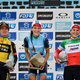 Lizzie Deignan (center) holding her trophy, a big granite cobblestone